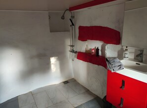 Un baño con ducha, lavabo y un armario rojo.