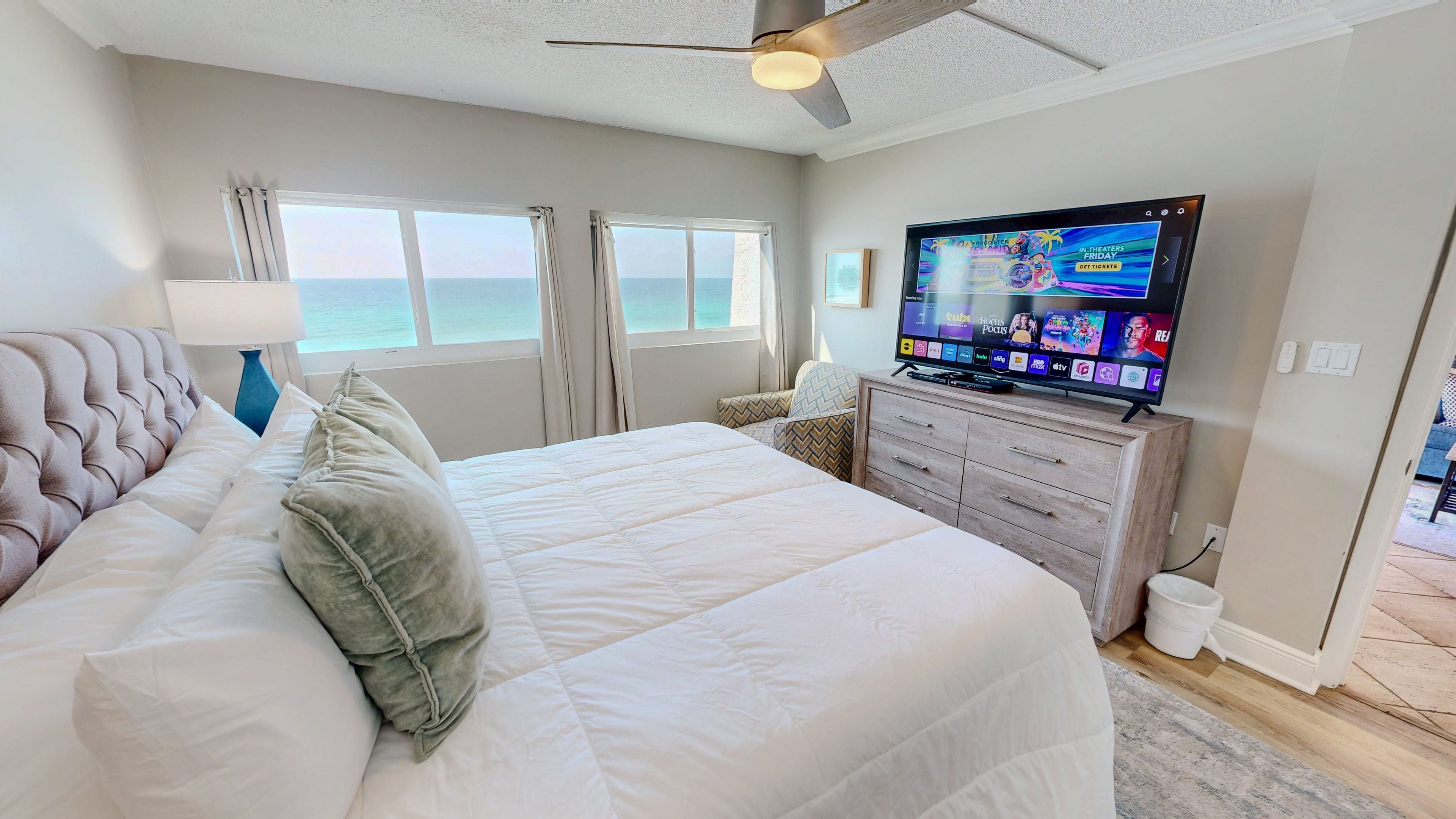 Une chambre à coucher avec un lit, une télévision, un ventilateur de plafond et une vue sur l’océan.