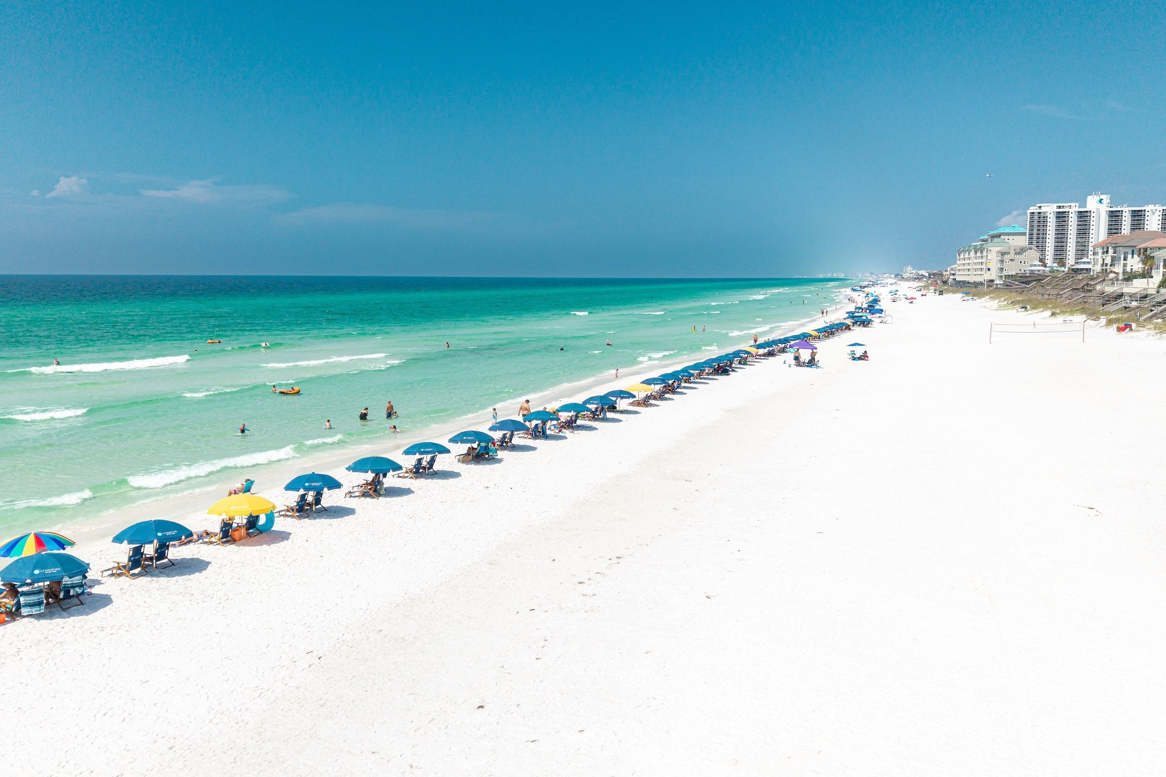 A beach with white sand and a row of umbrellas along the shore.