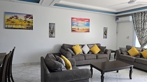 A living room with a grey sofa set, yellow cushions, a coffee table, and artwork on the walls. - Kijani Beach Homes Apartments Malindi (Malindi)