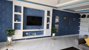 Una sala de estar con televisor de pantalla plana, estanterías blancas y plantas en macetas.