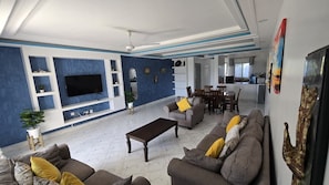 A modern living room with a flat-screen TV, sofas, a coffee table, and a dining area with chairs. - Kijani Beach Homes Apartments Malindi (Malindi)