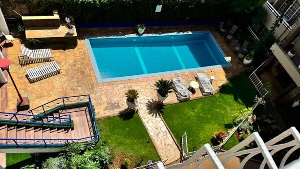 Una piscina rectangular con solárium de piedra, rodeada de sillas de descanso y plantas en macetas.