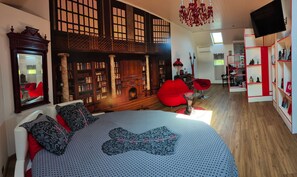 Une chambre à coucher avec un grand lit, un fauteuil rouge, une bibliothèque et un téléviseur.