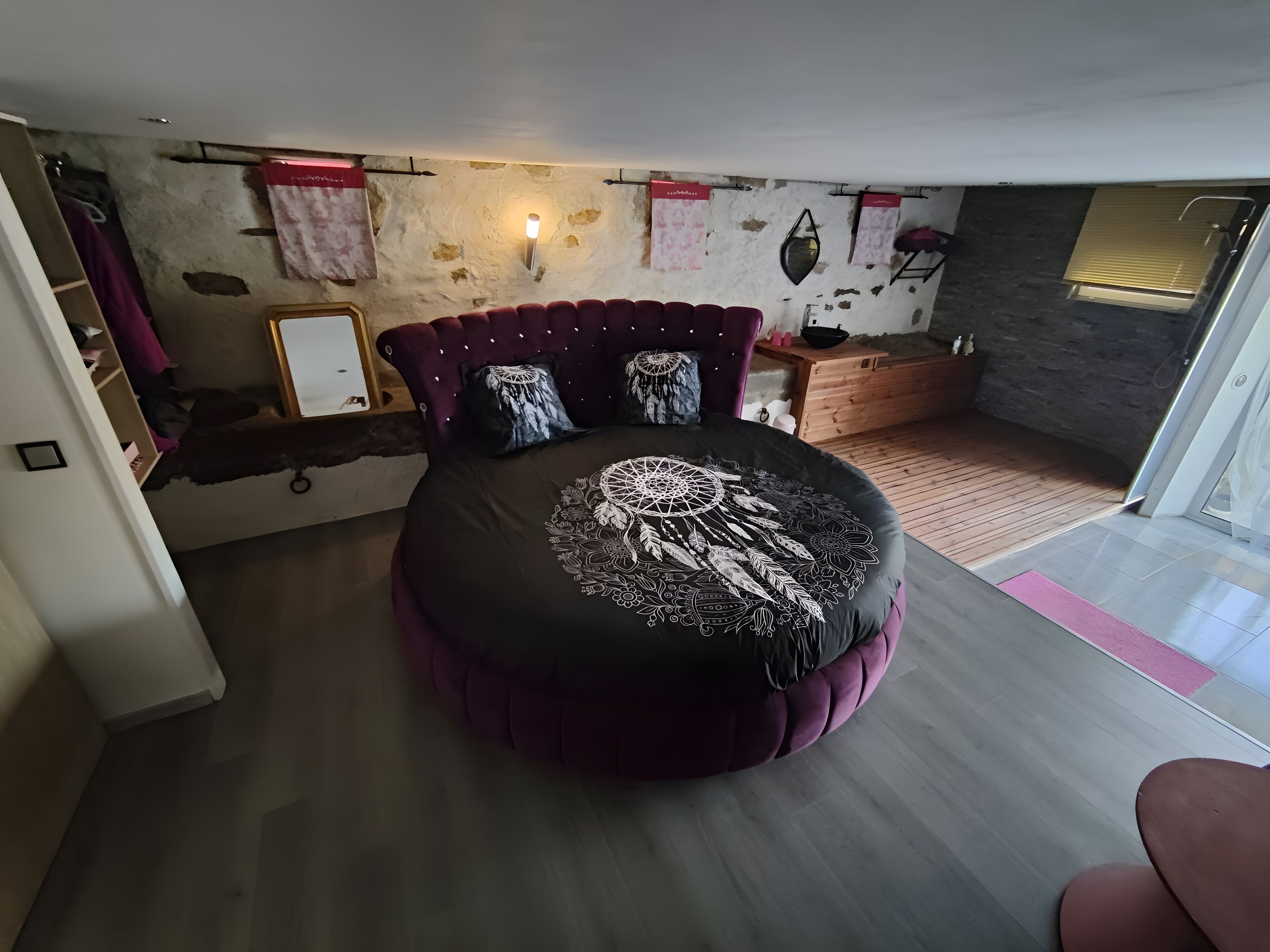 Une chambre à coucher moderne avec un lit rond, une commode en bois et un mur en pierre.