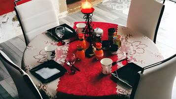 Une table à manger recouverte d’une nappe rouge, entourée de chaises, et agrémentée d’un centre de table composé de bougies.