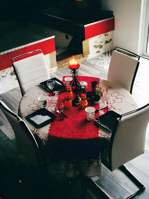 Une table à manger recouverte d’une nappe rouge, entourée de chaises, et agrémentée d’un centre de table composé de bougies.