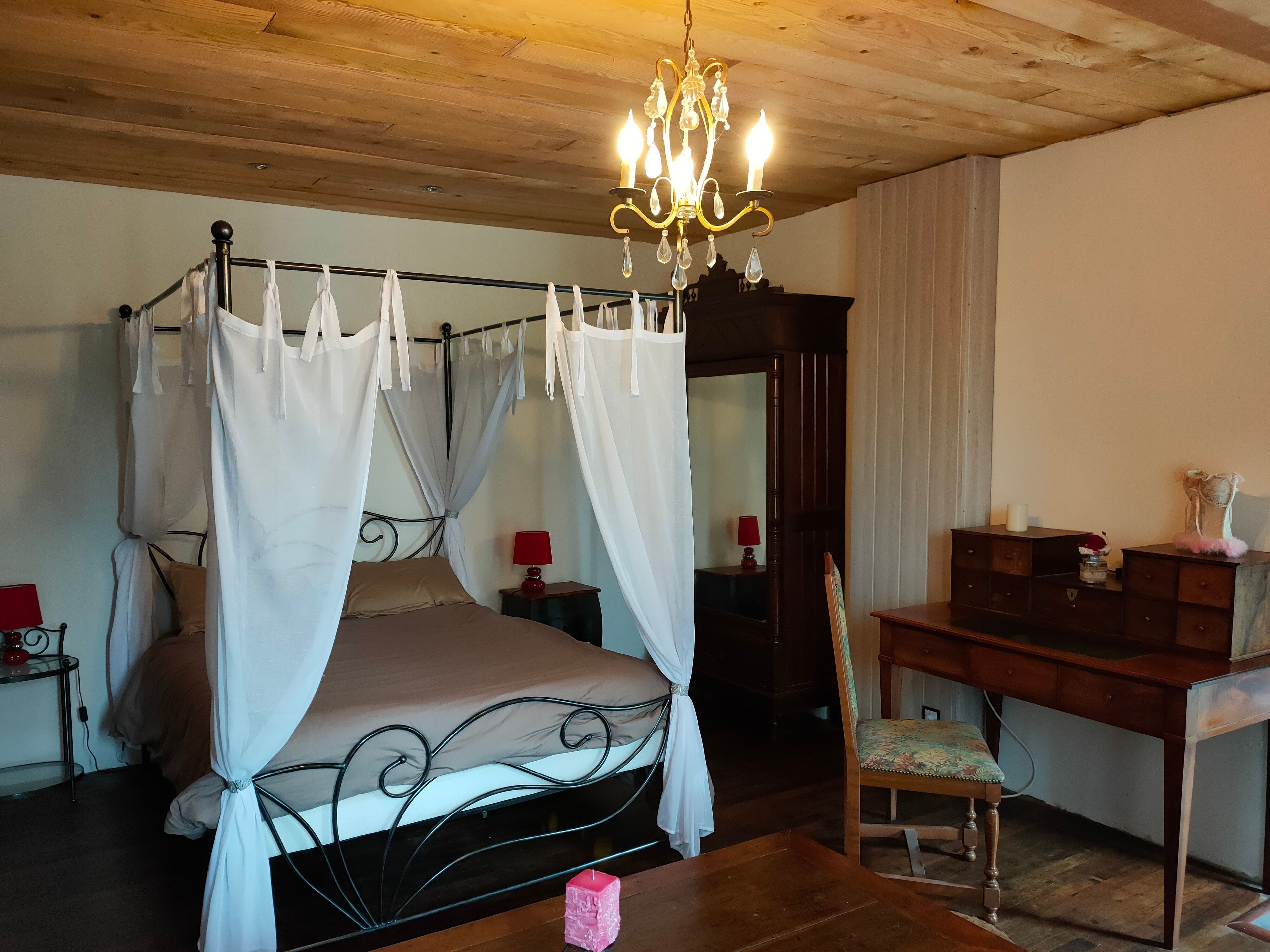 Un dormitorio con cama con dosel, un escritorio de madera, una silla, una araña y un espejo.
