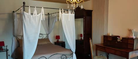 Un dormitorio con cama con dosel, un escritorio de madera, una silla, una araña y un espejo.