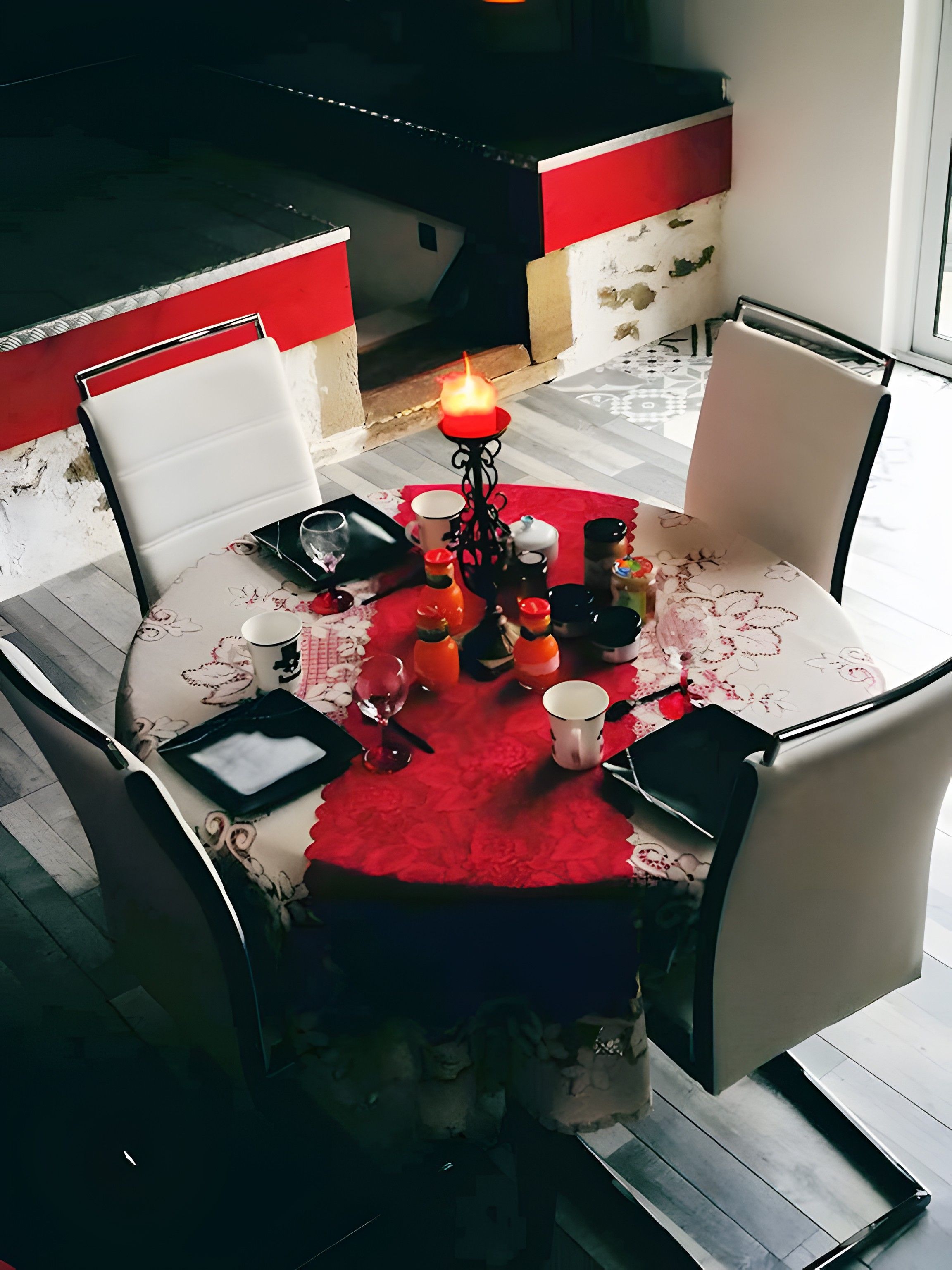 A dining table with a red tablecloth, surrounded by chairs, and a candle centerpiece.