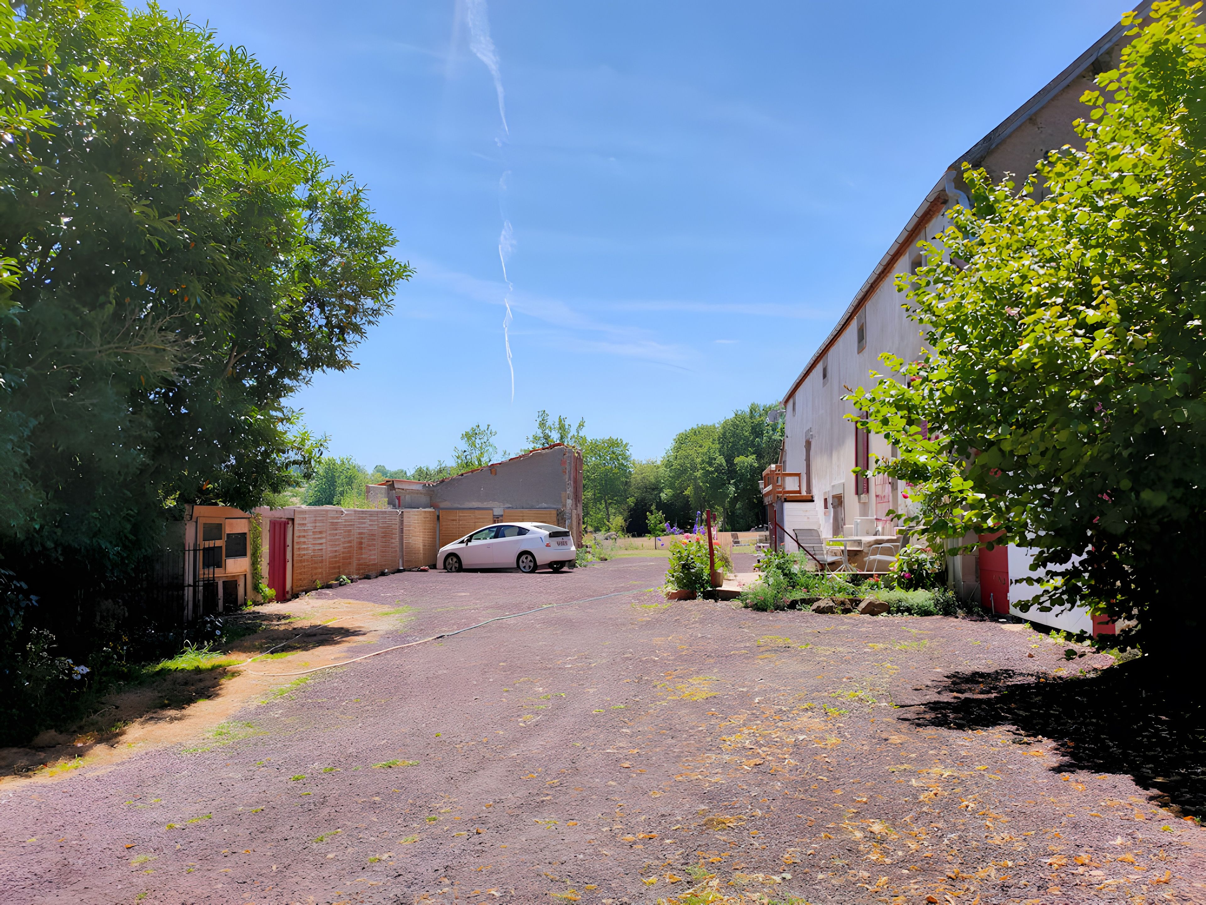 A gravel driveway leading to a white car parked in front of a building with a red door.