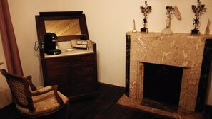 Une pièce comprenant une commode en bois, une chaise, une machine à café et une cheminée en marbre agrémentée d’objets décoratifs.