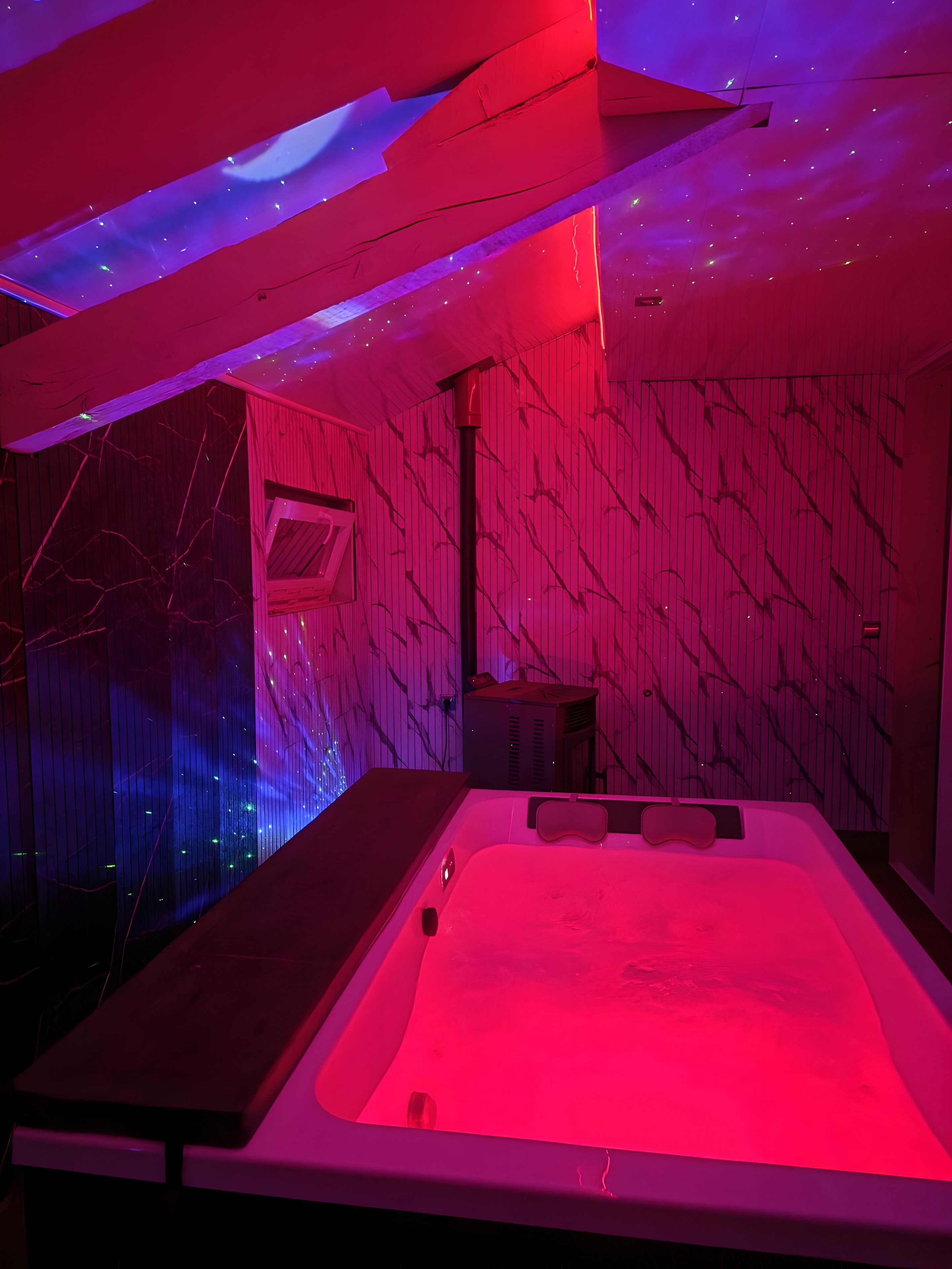 A room with a large bathtub, a small table, and a wall with a unique pattern.