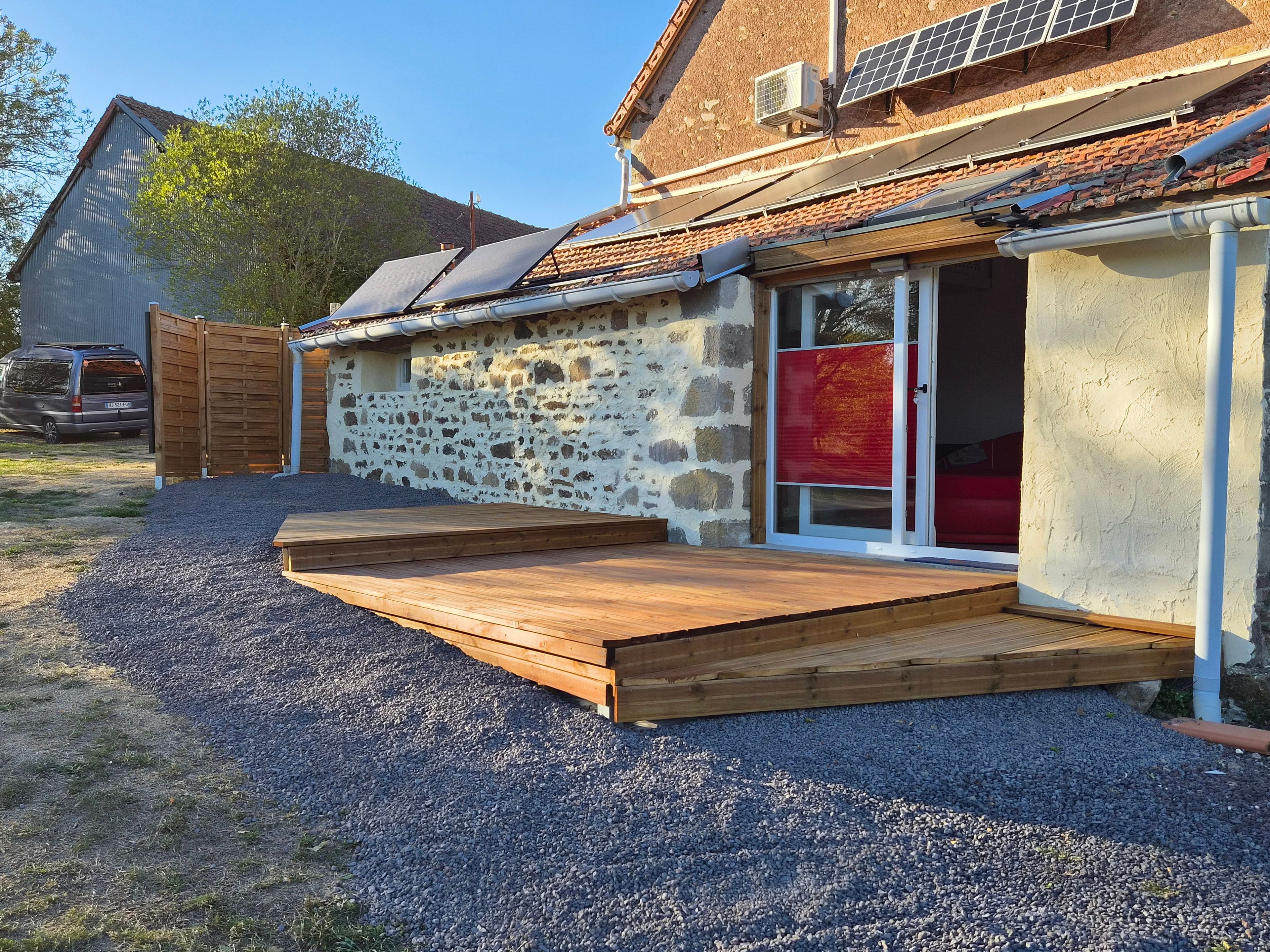 A house with a stone exterior, a wooden deck, and solar panels on the roof.