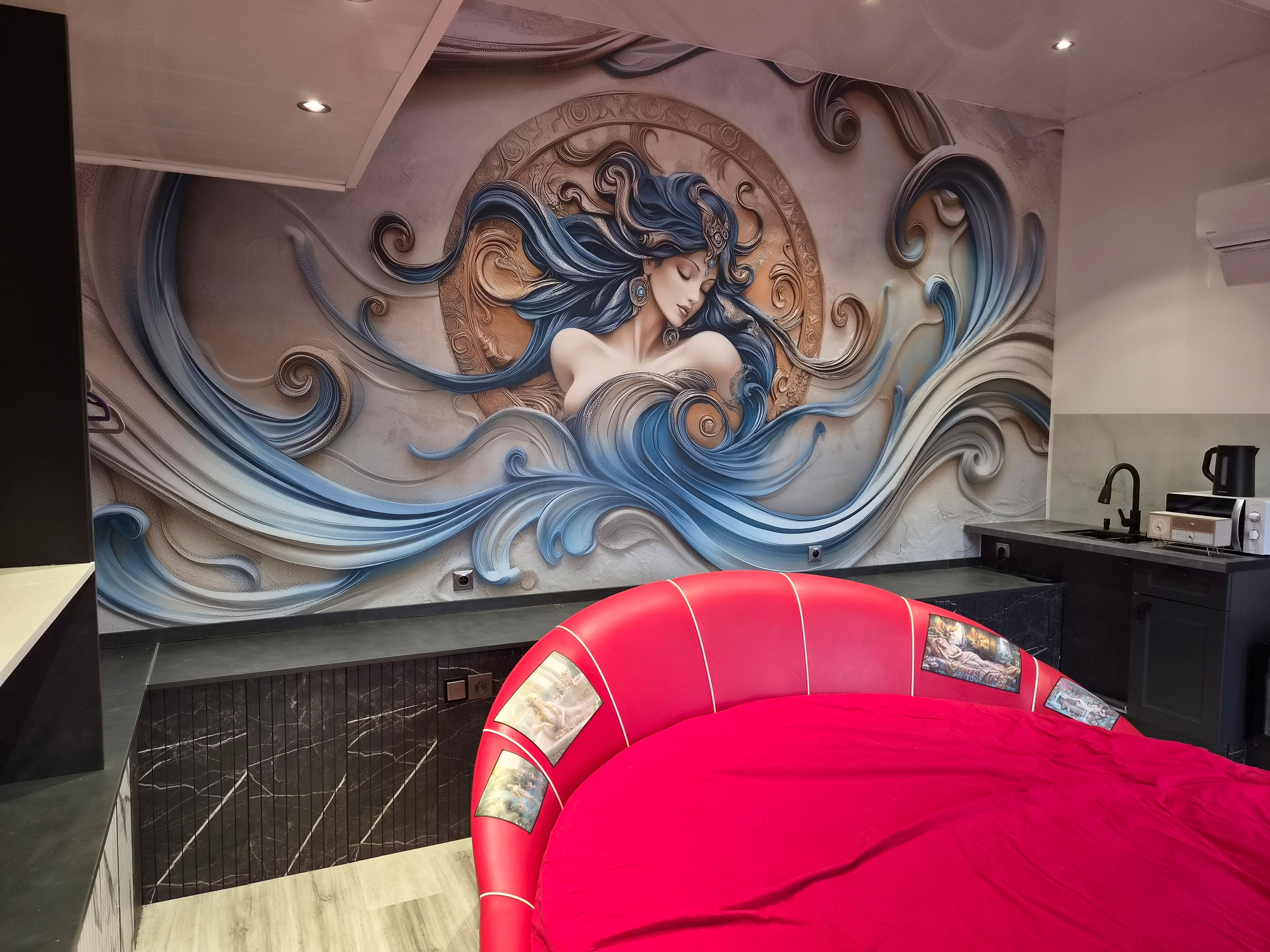 A modern interior with a mural, a red upholstered headboard, and a kitchen area.