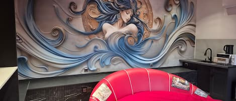A modern interior with a mural, a red upholstered headboard, and a kitchen area.