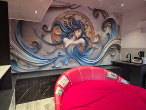 Een modern interieur met een muurschildering, een rode bekleden hoofdeinde en een keukenhoek.