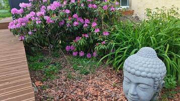 A garden with a Buddha head statue, a wooden deck, and flowering shrubs.