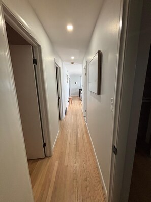A hallway with wooden flooring, white walls, and a ceiling light.