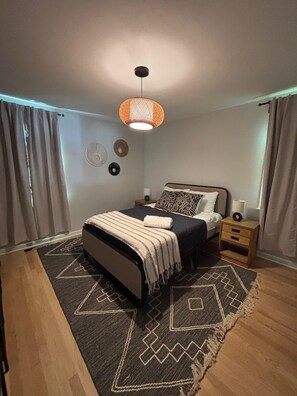 Ein modernes Schlafzimmer mit Bett, Nachttischen, einer Pendelleuchte und einem gemusterten Teppich.