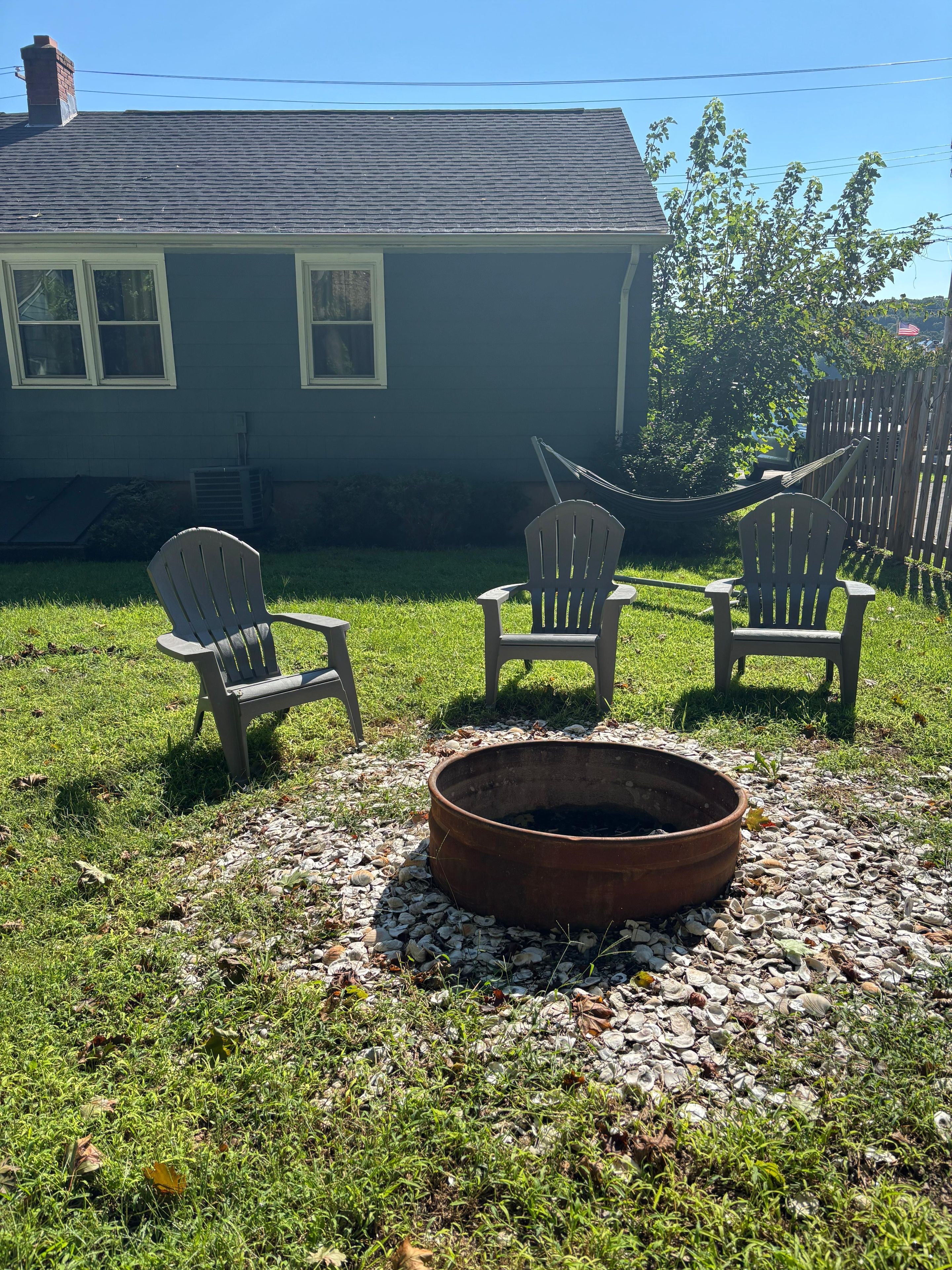 Un patio trasero con un brasero, dos sillas Adirondack y una casa al fondo.