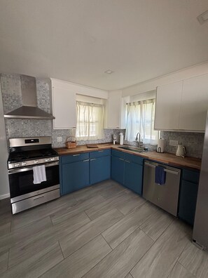 Een moderne keuken met een roestvrijstalen fornuis, blauwe kastjes en een houten aanrecht.