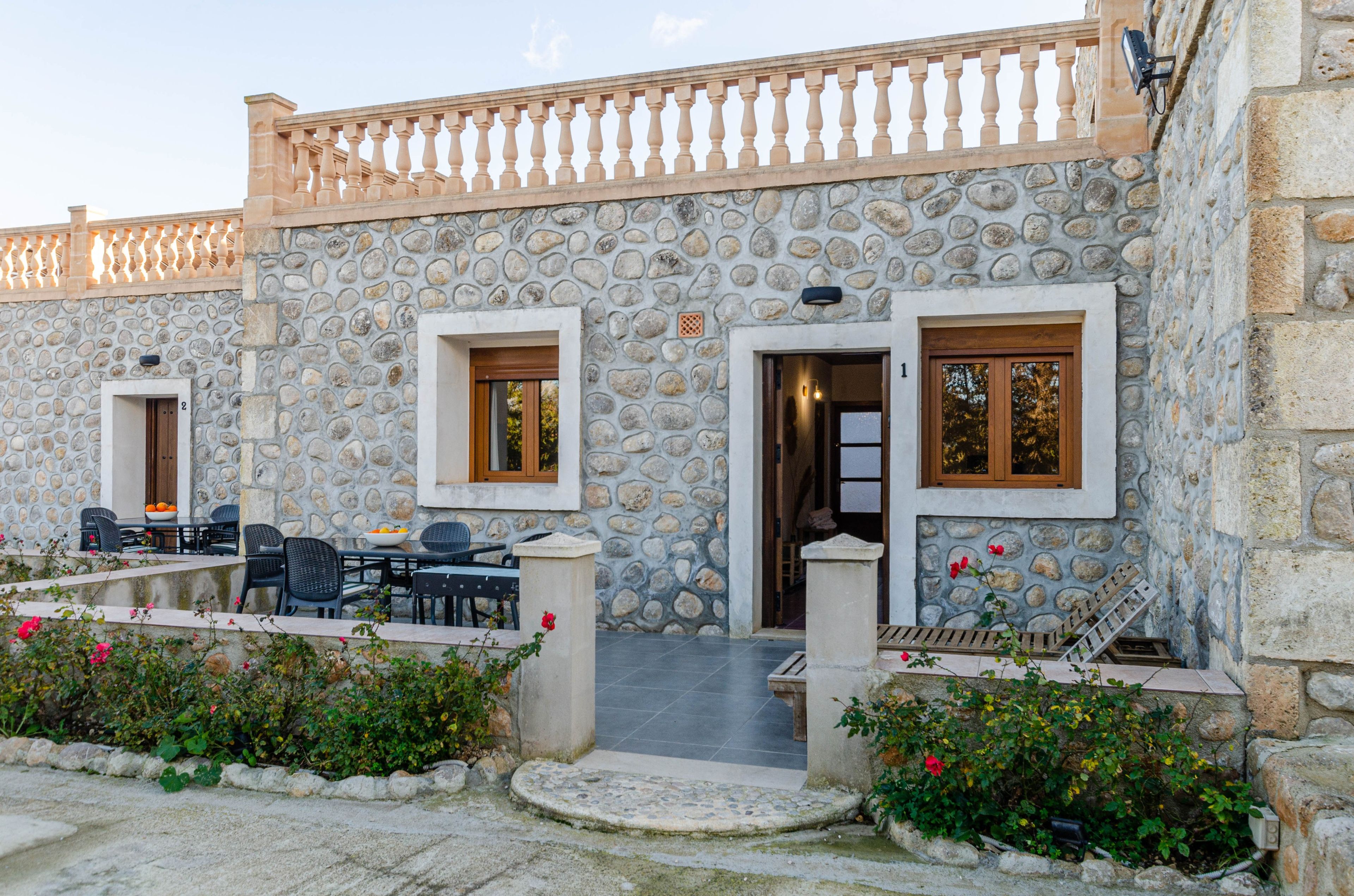 Un edificio de piedra con dos puertas, cada una con un ventanal, y un balcón con mesas al aire libre.