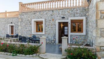 Un edificio de piedra con dos puertas, cada una con un ventanal, y un balcón con mesas al aire libre.