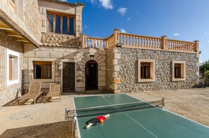 A courtyard with a tennis court, stone walls, and a wooden balcony.
