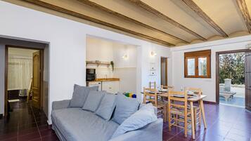 A living room with a grey sofa, wooden dining table, and chairs. There is a kitchen area with a microwave and cabinets.