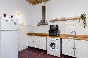 Une cuisine compacte équipée d’un réfrigérateur, d’un four à micro-ondes, d’un lave-linge et d’un évier.