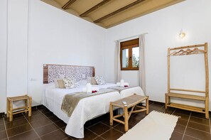 Un dormitorio con una cama grande, dos mesitas de noche, un banco de madera, un perchero y una ventana con cortinas.
