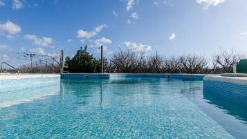 A clear blue swimming pool with tiled edges, surrounded by a fence and trees.