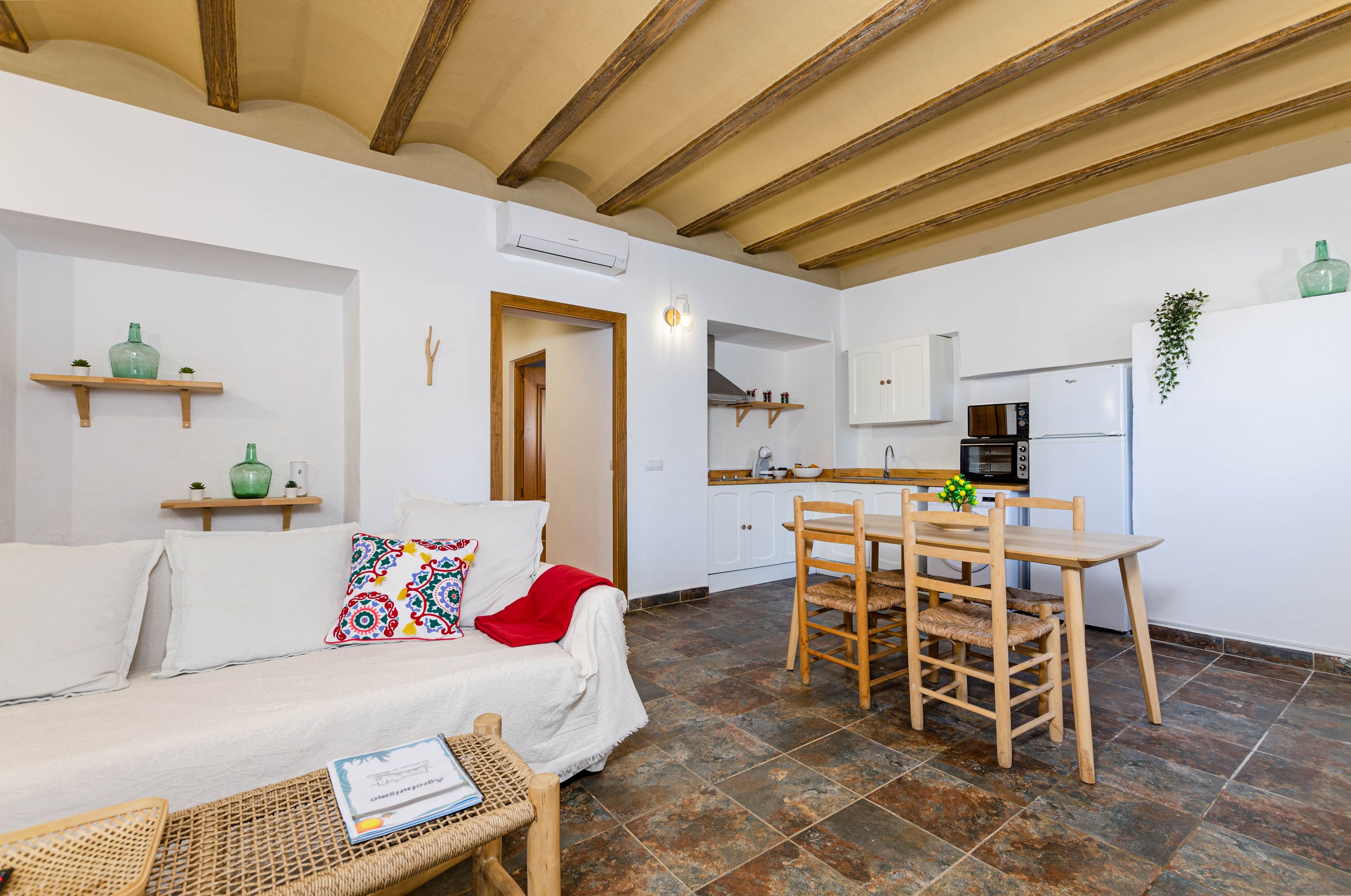 Un espacio habitable compacto con sofá, una mesa de comedor con sillas, una zona de cocina y un pequeño balcón.