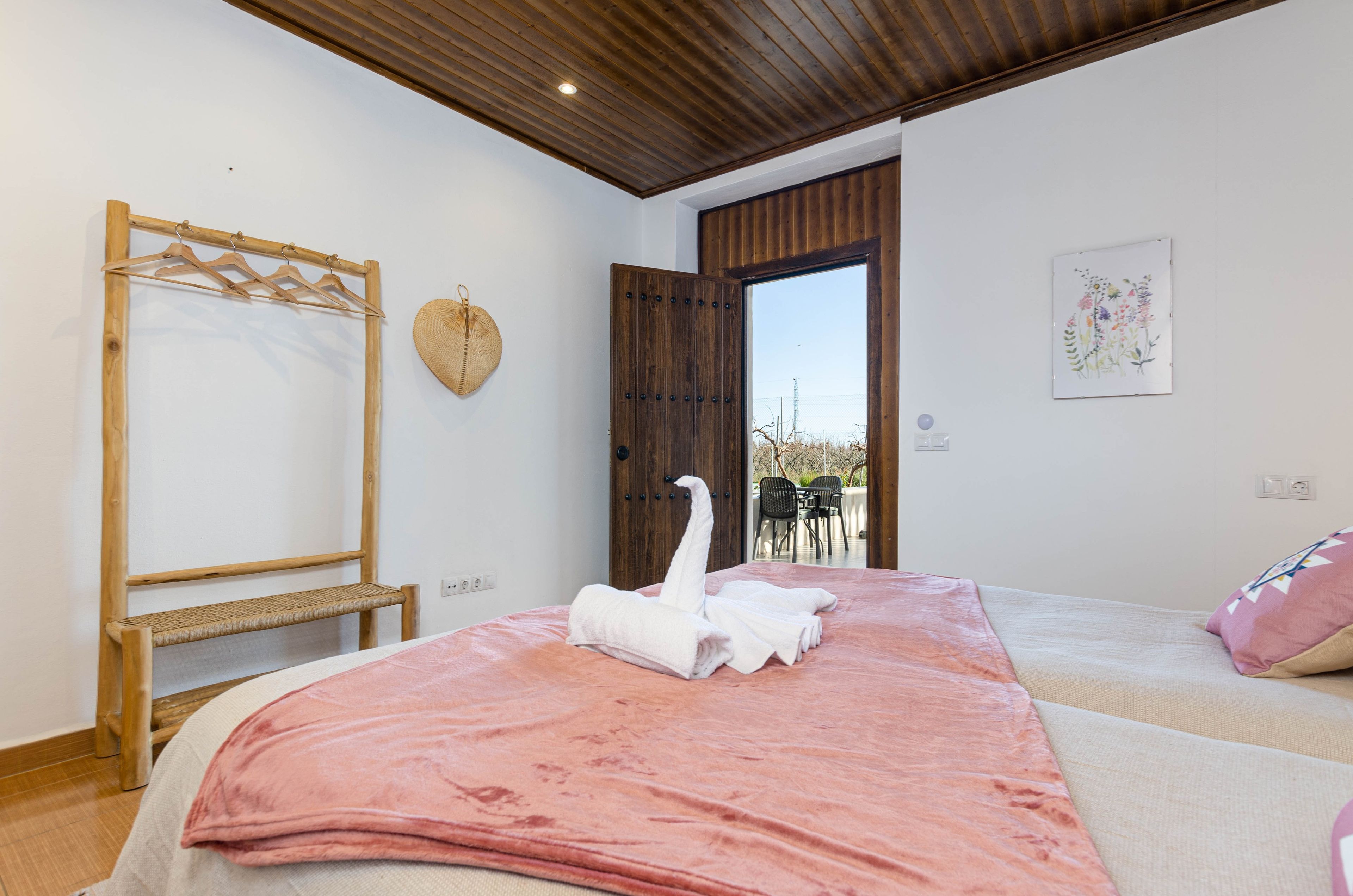 A bedroom with a bed, a wooden headboard, a hanging basket, and a view of the outside.