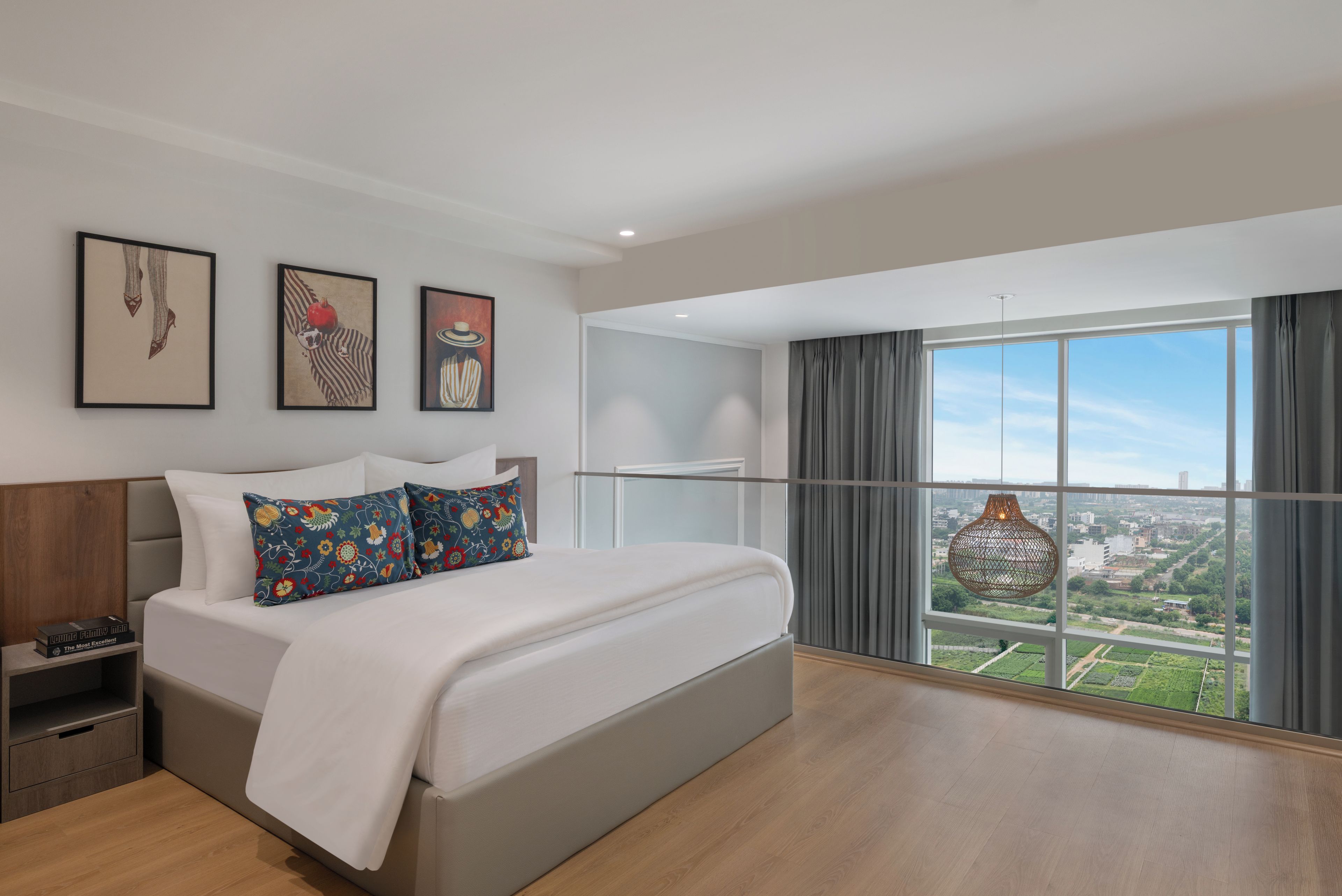 Una habitación de hotel moderna con una cama grande, una mesita de noche, un ventanal con vistas y obras de arte en la pared.