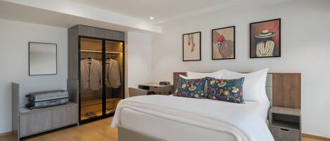 A modern bedroom with a large bed, a walk-in closet, and three framed artworks on the wall.