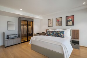 A modern bedroom with a large bed, a walk-in closet, and three framed artworks on the wall. - ONE Atmosphere Suites - Corner Walk (Gurugram)