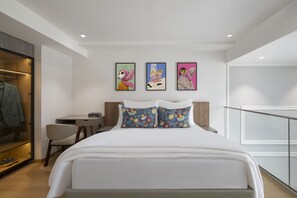 Una habitación de hotel moderna con una cama, un escritorio y una silla. Hay tres obras de arte enmarcadas en la pared.