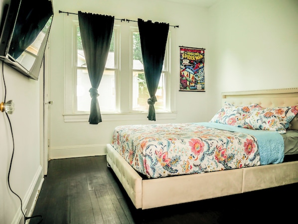 Un dormitorio con cama, una ventana con cortinas, un cartel en la pared y una puerta.