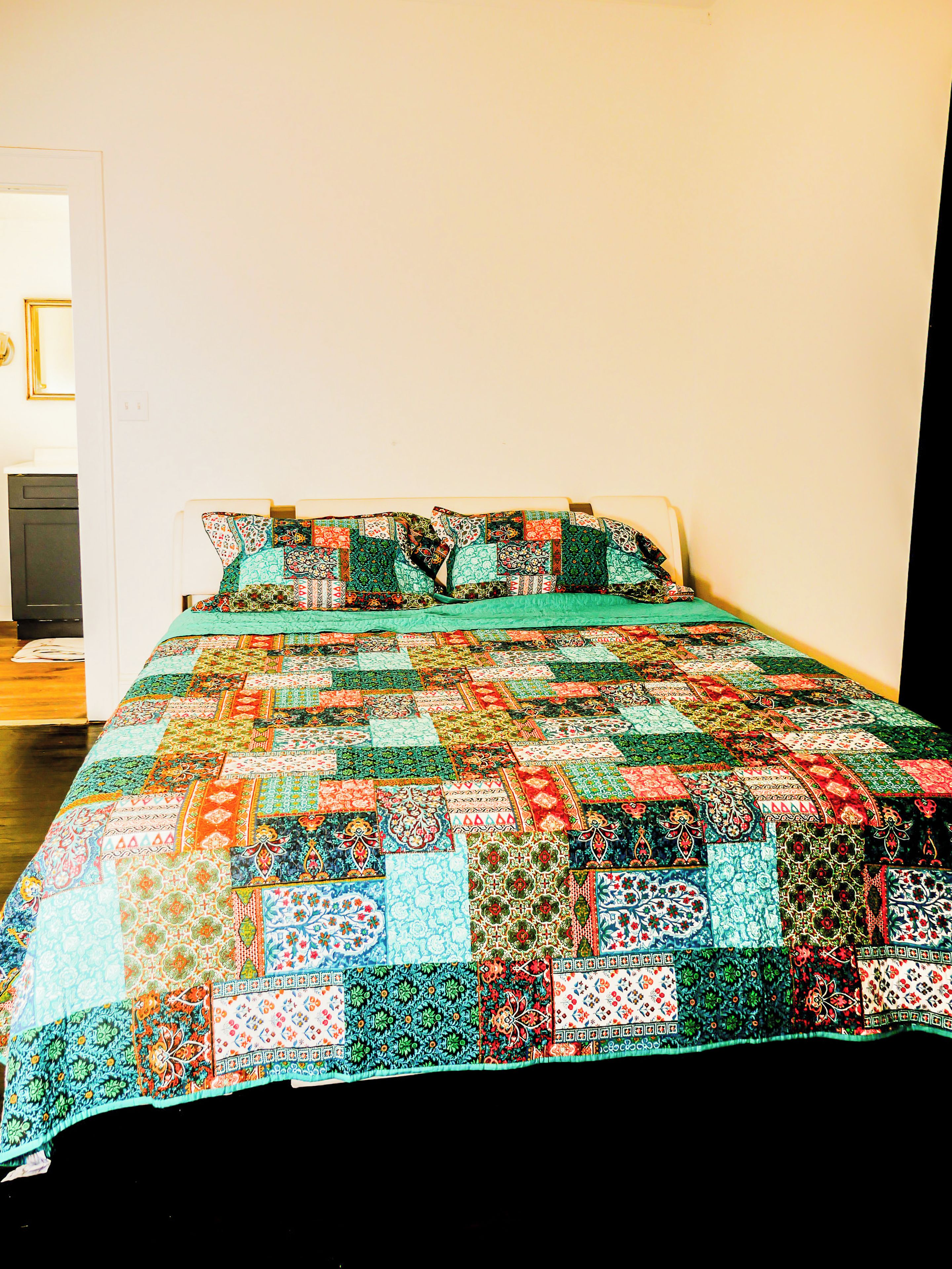 A bed with a colorful quilt and pillows, a white wall, and a door.