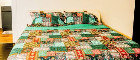 A bed with a colorful quilt and pillows, a white wall, and a door.