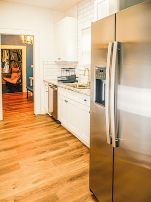 Una cocina moderna con gabinetes blancos, un refrigerador de acero inoxidable y piso de madera.
