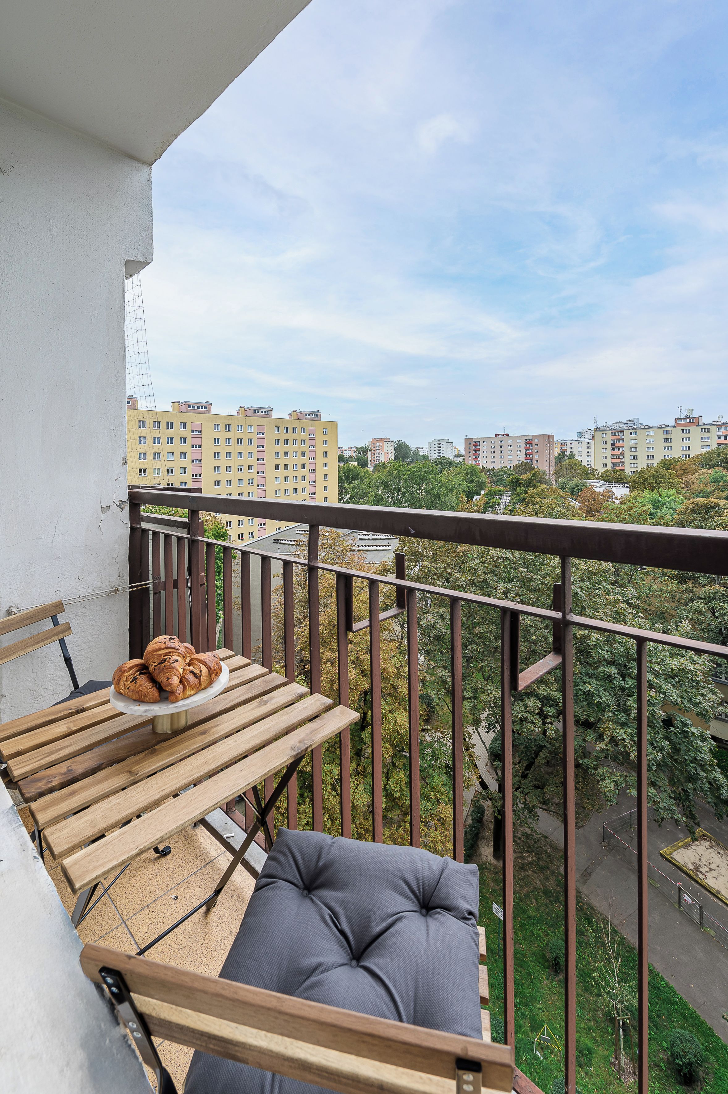 A balcony with a wooden table, two croissants, and a grey cushion.