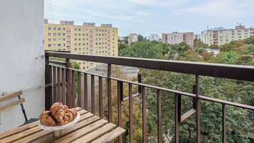 A balcony with a wooden table, two croissants, and a grey cushion.
