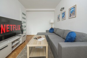 Uma sala de estar moderna com televisão de tela plana, sofá cinza e uma mesa de centro.