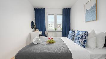 A hotel room with a bed, a desk, a chair, a window with curtains, and a wall-mounted picture.