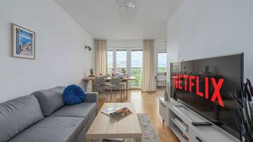 A modern living room with a grey sofa, a coffee table, a flat-screen TV, and a dining area with a table and chairs.