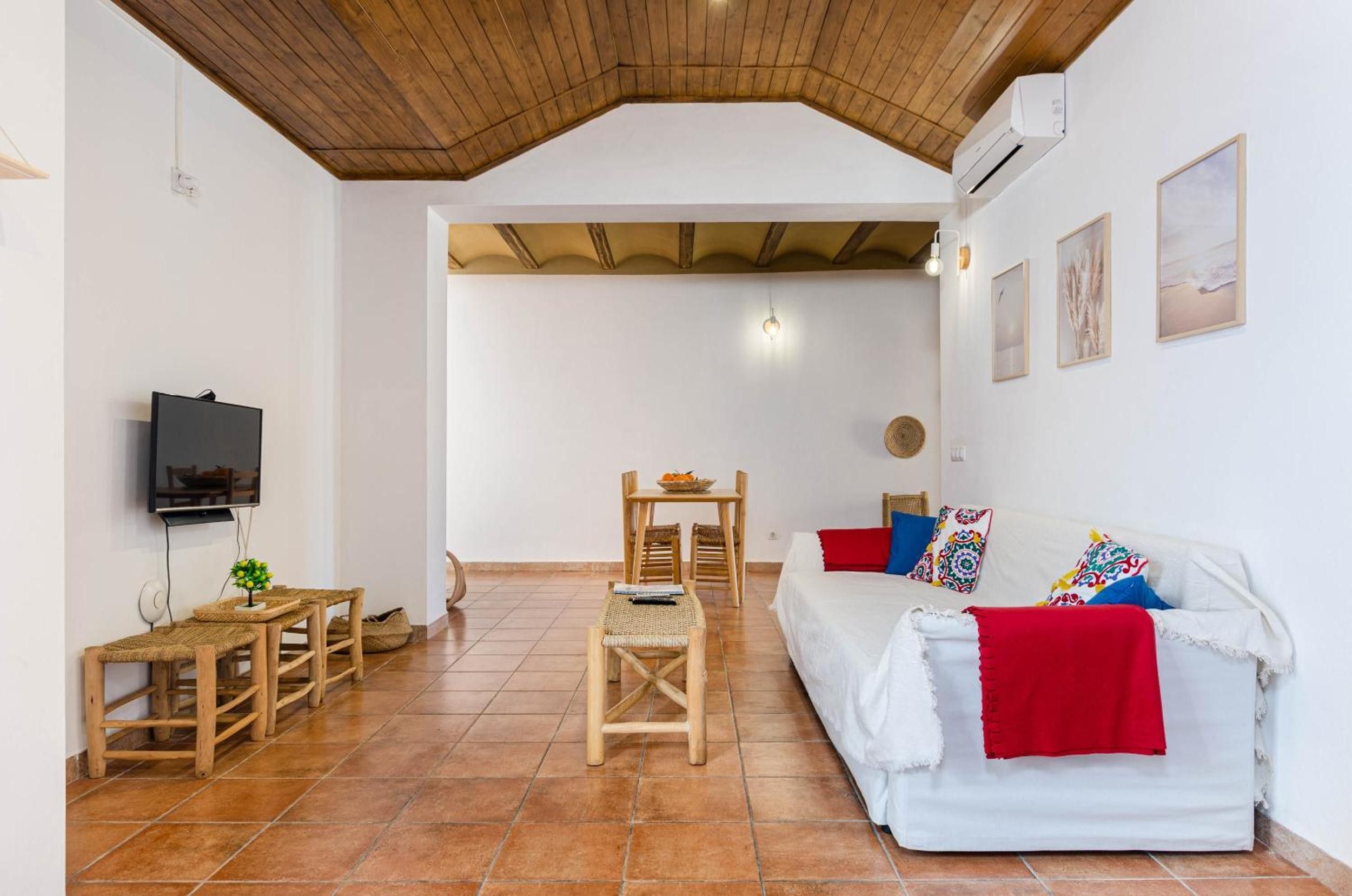 Una sala de estar amoblada con techo de madera, un sofá, un televisor y una zona de comedor con mesa y sillas.