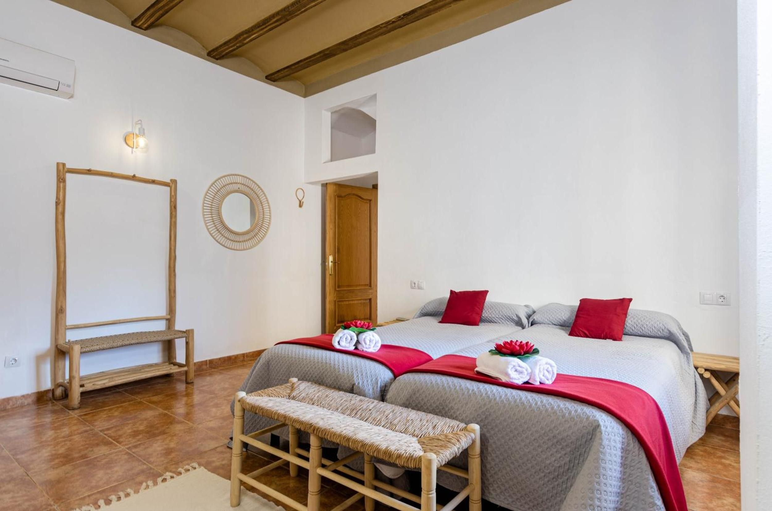 Habitación de hotel con dos camas, un banco de madera, un espejo y una puerta que da a otra habitación.